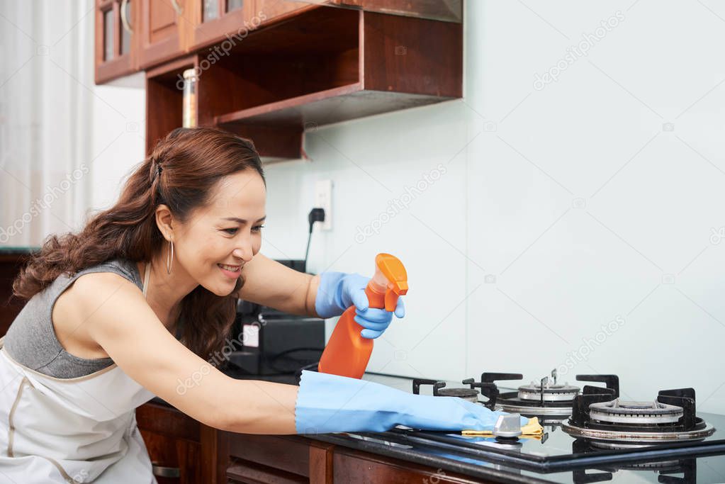Housewife spraying stove with detergent before wiping it