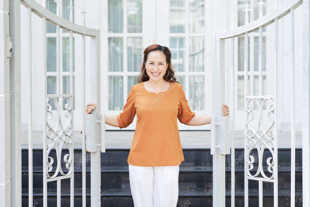 Happy pretty Vietnamese woman opening steel gates of her house