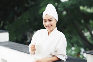 Gülümseyen güzel Vietnamca kadın bornoz ayakta açık havada kahve ile