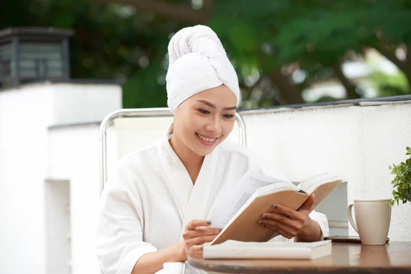 亚洲年轻女子在浴袍阅读书后的水疗程序 — 图库照片