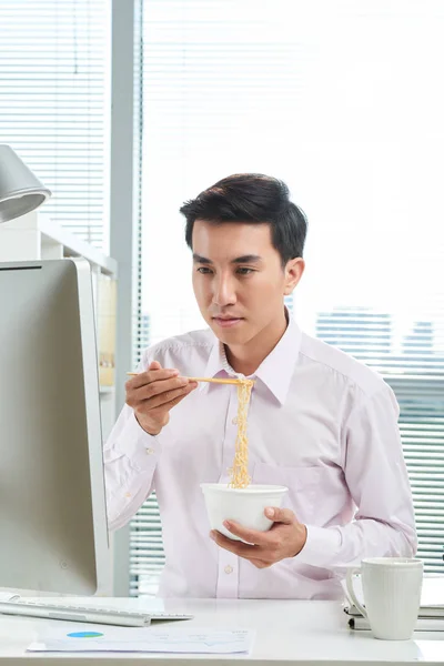 越南青年商人在电脑屏幕上阅读电邮及吃方便面 — 图库照片