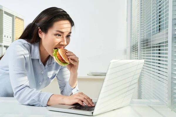 兴奋的越南商务女士吃汉堡包和检查笔记本电脑屏幕上的电子邮件 — 图库照片