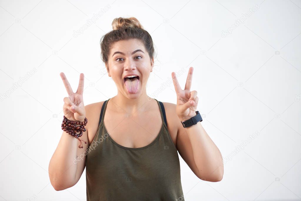 Portrait of pretty young woman sticking out tongue and showing victory gesture