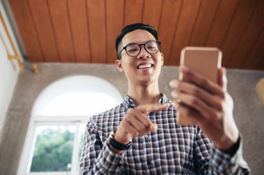 Mutlu bir şekilde smartphone içinde video sohbet yaparken gülümseyen yakışıklı Asyalı gencin düşük açılı görünüş