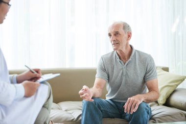 Yaşlı adam kanepede oturan ve şikayetler doktor ile ev ziyareti sırasında paylaşımı
