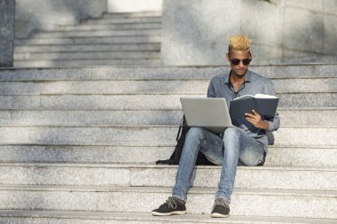 Basamaklarında oturan ve dizüstü bilgisayarda ödev üniversite öğrencisi