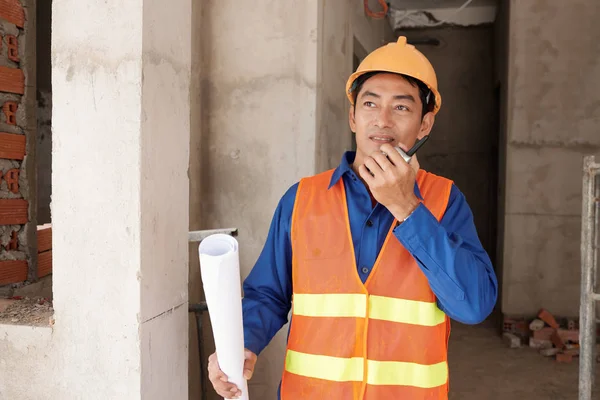 Asian contractor in hard hat controlling work with walkie-talkie