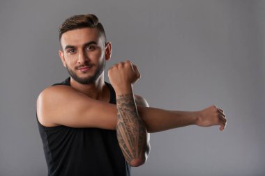 Dövmeli gri arka plan üzerinde el kasları germe sırasında kameraya gülümseyen yakışıklı genç sporcu 