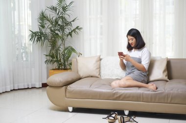 Asyalı esmer kız koltukta istirahat ve oturma odasında cep telefonu kullanma