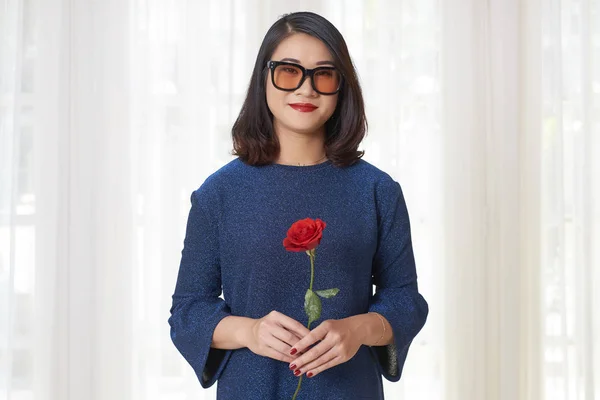 ファッション眼鏡や青いドレスの赤いバラを押しながらカメラ目線でアジアのかわいい女の子の肖像画 — ストック写真