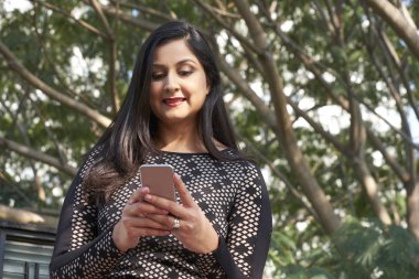 Zaman açık havada ayakta smartphone uygulama kullanarak pozitif çok Kızılderili kadın