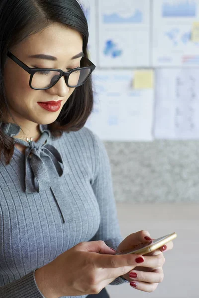 眼鏡立っていると オフィスで彼女の携帯電話でメッセージを入力しての若い美しい女性実業家 — ストック写真