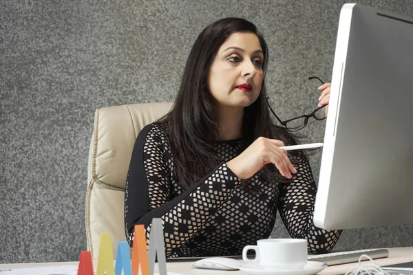 Middle-aged businesswoman taking off glasses to read e-mail on computer screen