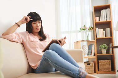 Güzel genç Vietnamlı kadın kanepede oturan ve kitap okuma