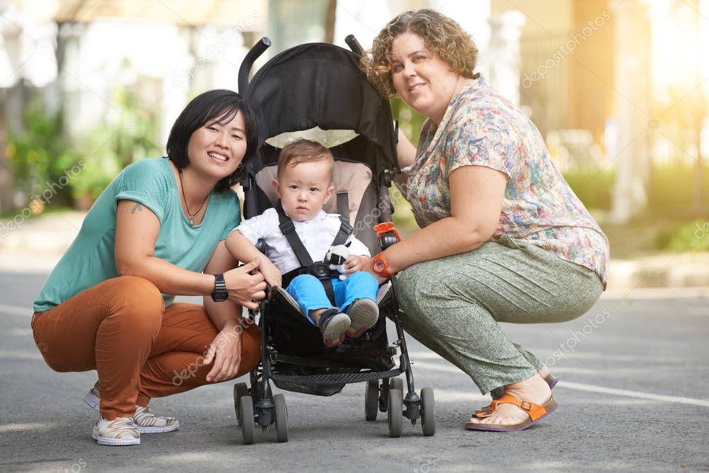 Cheerful homosexual couple with child in stroller spending time outdoors