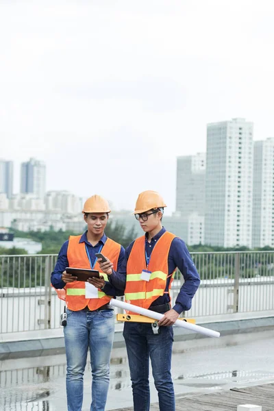 亚洲年轻建筑工人在平板电脑和智能手机上安装工作应用程序 — 图库照片