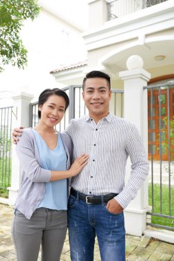 Genç Asyalı karı koca kamera, arka planda yeni evlerine gülümseyen