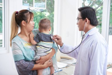 Asya genç anne onu yürümeye başlayan çocuk erkek çocuk doktoru ona steteskop ile dinleme sırasında kollarındaki holding