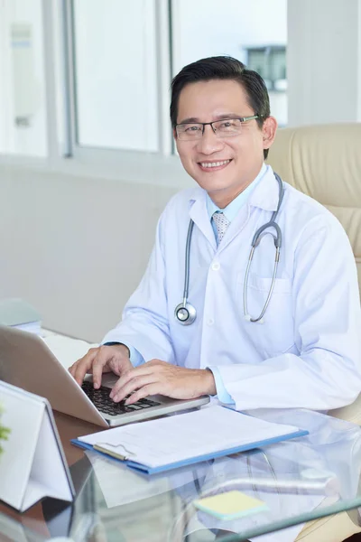 Portret Azjatycki Lekarz Fartuchu Siedzi Jego Miejscu Pracy Laptopem Uśmiechając Obrazek Stockowy