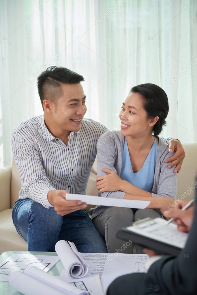 Cheerful young Asian couple meeting with estate agent and discussing documents