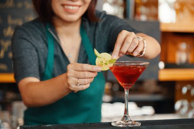 Smiling bartender putting lime slice on rim of cherry margarita glass clipart