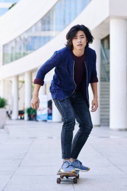 Yakışıklı genç Asyalı adam şehirdeki sokak kaykay sürme