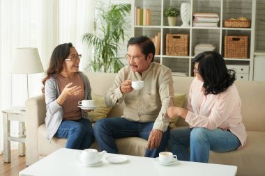 Aged Vietnamese people drinking tea and discussing news at home clipart