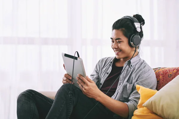 Handsome Vietnamese man with bun hairstyle wearing headphones when watching video on tablet computer