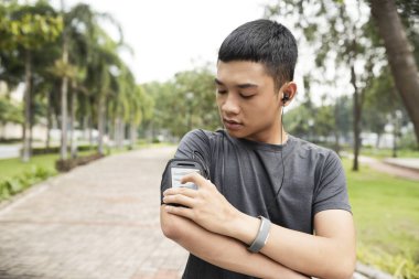 Yakışıklı genç Asyalı adam onun smartphone değişen Müzik kanalındaki Park'ta jogging önce 