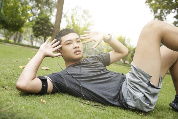 夏の公園で腹筋運動を行うときに音楽を聴く若いベトナム人男性 — ストック写真