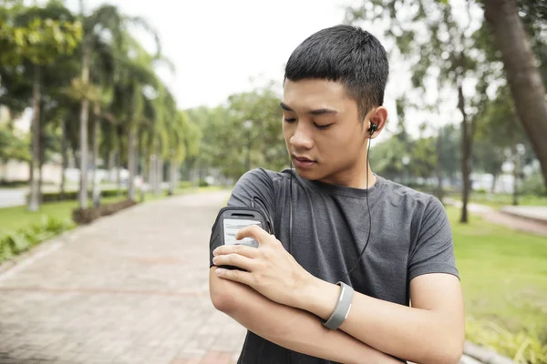 アジア系のハンサムな若い男は公園でジョギングする前に彼のスマート フォンに変化する音楽トラック — ストック写真