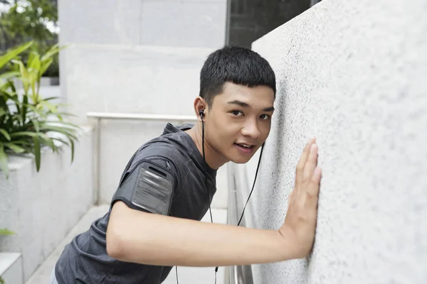 Smiling young Asian man doing wall push-ups outdoors