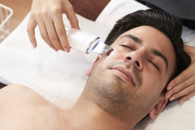 Ziyaret güzellik uzmanı ve Başlarken ultrason peeling yüzünde genç yakışıklı adam 