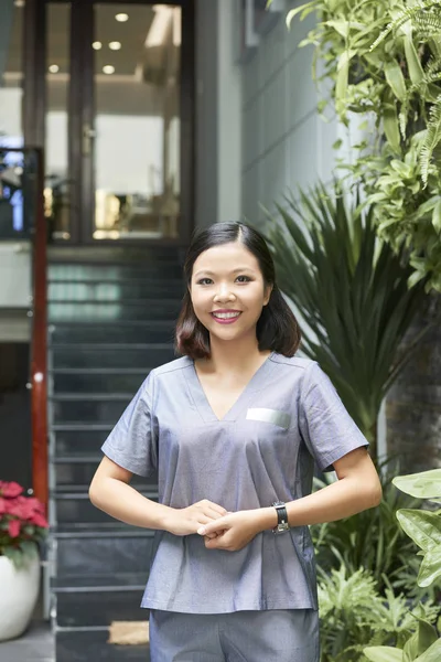 Portrait of Asian young woman in uniform standing outdoors near the entrance to wellness center
