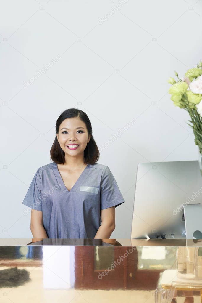 Portrait of Asian woman in uniform standing at her workplace at reception smiling in wellness center