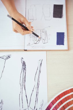 Anonim terzi el atış yukarıdan kalem tutan ve yapım kumaş örnekleri yakınındaki açık not defteri stüdyoda çalışırken skeçler