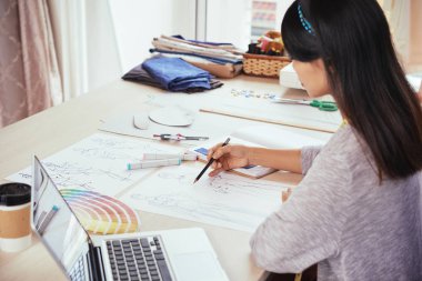 Genç erkek yan görünüm terzi dizüstü yakınındaki masada oturan ve stüdyoda çalışırken çizim