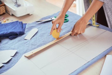 Anonim moda tasarımcısı studio terzilik çalışırken mavi kumaş üzerine tebeşir ve anahat kağıt deseni için cetvel kullanarak