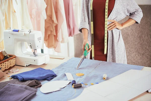 匿名ファッションデザイナー持株鋭いハサミとワーク ショップを仕立てで作業中の青い布でテーブルの近くに立って — ストック写真