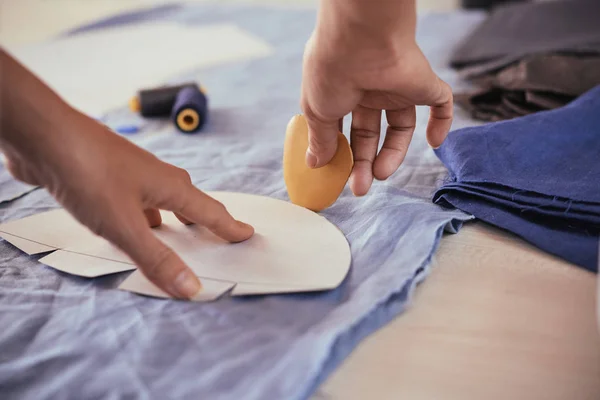 匿名裁缝的手特写镜头拍摄 用粉笔轮廓纸图案在桌子上的蓝色布在工作室 — 图库照片