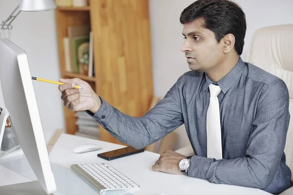 认真的印度企业家在分析报告中的数据时 用笔指着电脑屏幕 — 图库照片