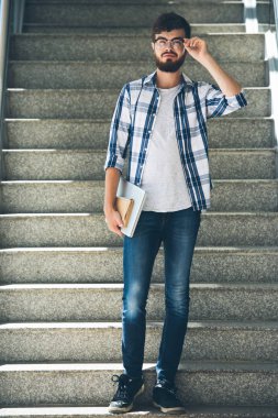 Kitap ve dizüstü bilgisayar gözlük ayarlama ve kamera bakarak kolej öğrencisi