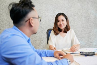 Genç Asyalı kadın ve adam ofiste masada kağıtlar ile çalışma ve iletişim 