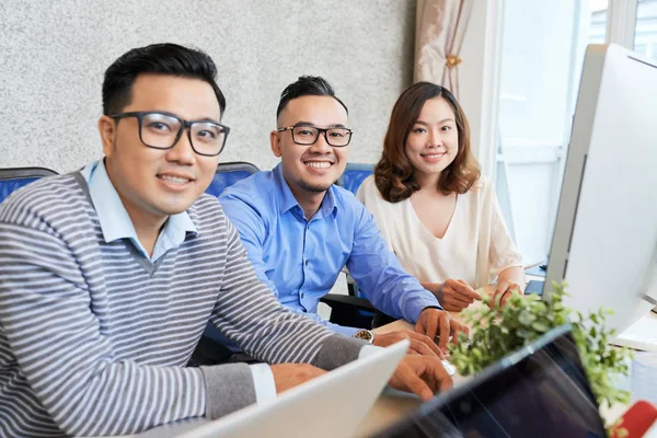 亚洲妇女和男子坐在办公桌前 办公室里有电脑 对着镜头微笑 — 图库照片