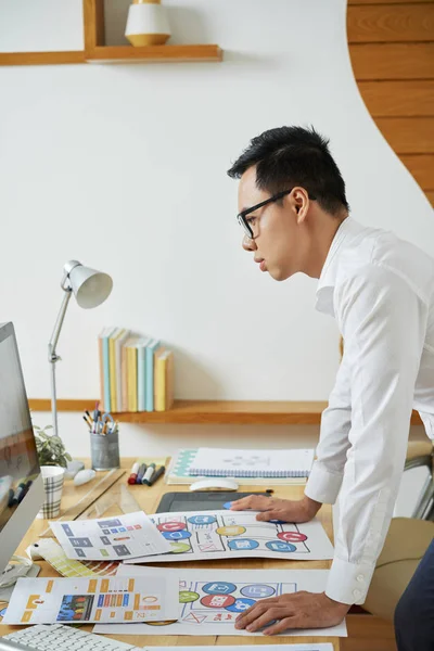 Professional graphic designer leaning to table to check colors of logotype on computer screen