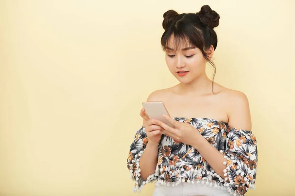 漂亮的时尚亚洲女人与发面包冲浪智能手机在浅黄色背景 — 图库照片