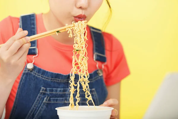 黄色の背景にお箸で食べながら温麺に吹いてカジュアルな女性のショット作物 — ストック写真