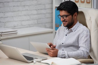 Tablet bilgisayarda haber okurken gülümseyen yakışıklı genç Hintli işadamı