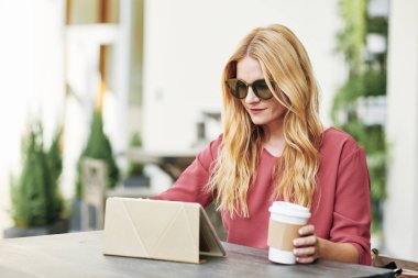 Gülümseyen güzel kadın güneş gözlüğü, eve servis kahve ve tablet bilgisayar üzerinde çalışıyor
