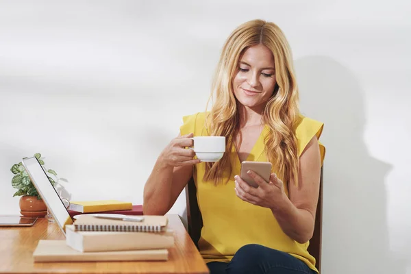 Vrij Lachende Vrouw Drinken Thee Lezen Van Berichten Haar Telefoon — Stockfoto